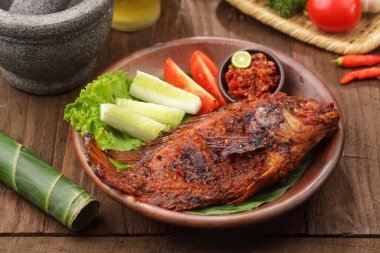 Kahverengi tabakta taze sebze ve acılı sosla birlikte ızgara balık.