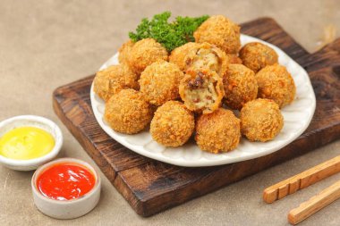 Tahtada sunulan maydanozla süslenmiş altın kızartma topları.