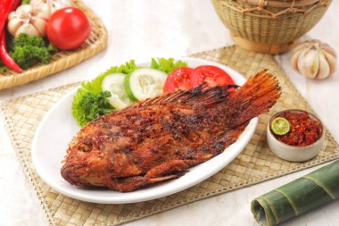 Beyaz masada taze sebzelerle servis edilen ızgara balık tabağı.