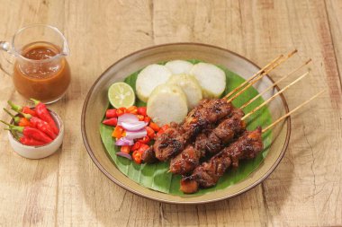 Dilimlenmiş sebze ve sosla servis edilen ızgara et şişleri.