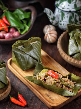 Tahta tabağa sebzelerle sarılmış yeşil yapraklara sarılı renkli bir yemek.