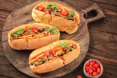 Üç sosisli, sebze ve ahşap kesim tahtasının üstünde sos.