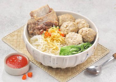 İçinde et, balık köftesi, sebze ve dokuma hasırı sosu olan bir kase erişte.