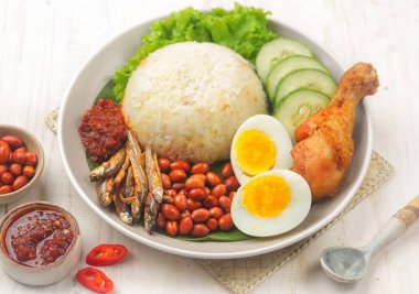 Tavuk budu, haşlanmış yumurta, salatalık ve baharatlı sambal ile servis edilen bir tabak pirinç.