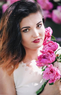 Güneş ışığında pembe şakayık tutan parlak makyajlı güzel bir genç kadının yakın plan portresi..