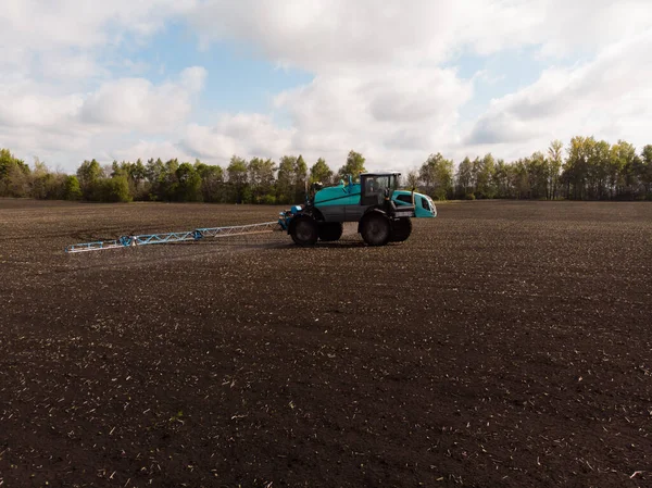 Pekerjaan pertanian musim semi di ladang. Traktor menyemprot tanaman dengan herbisida, insektisida dan pestisida. Stok Lukisan  