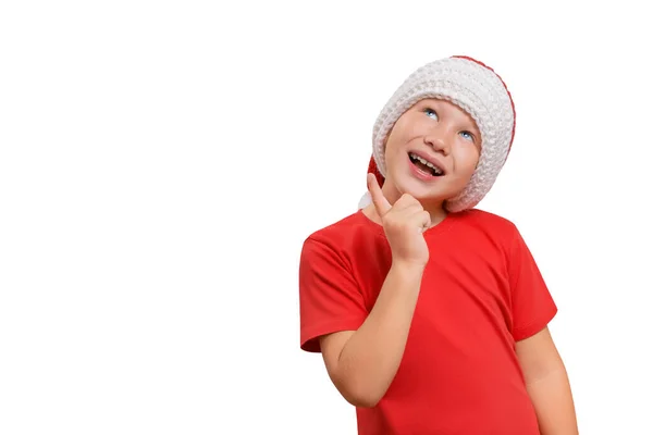 赤いTシャツとニットのサンタの帽子を着たハンサムな陽気な白人の少年は 思慮深く見上げ コピースペースと白い背景に隔離されたクリスマスプレゼントの夢を見ます アイデア 意思決定の概念 — ストック写真