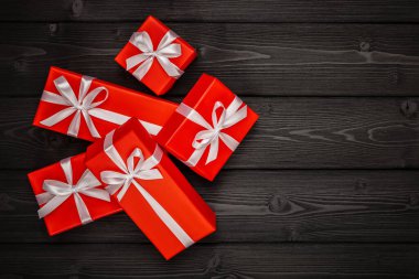 Beyaz kurdeleli kırmızı ambalaj kağıdında zarif hediyeler ve siyah ahşap arka plan manzaralı fiyonklar. Boşluğu kopyala.