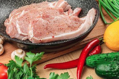 Koyu bir tavada taze çiğ et parçaları. Mantar, maydanoz, dereotu, domates, yeşil soğan, limon ve acı biberin yanında kesim tahtasının arka planında baharatlar var. Yakın plan. Yukarıdan görünüm