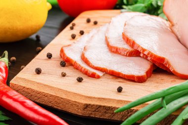 Füme, sulu, iştah açıcı et, göğüs eti, ahşap bir tahtada ince ince dilimler halinde doğranmış jambon. Yakınlarda karabiber, kırmızı biber, limon ve yeşil soğan var..