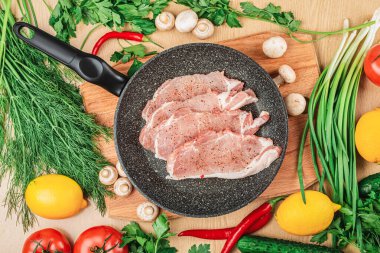 Kızartma tavasında baharat bulunan dilimlenmiş çiğ domuz eti ve ahşap tahta manzarası. Masanın üzerinde limon, domates, acı biber, mantar, yeşil soğan ve maydanoz var..