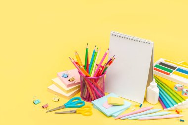 Makas, defterler, bardaktaki kalemler, yapıştırıcı, plasticin, sivri uçlu kalemler, parlak sarı arka planda ataçlar. Uzayı kopyala Reklam, tasarım, Mükemmel rötuş.