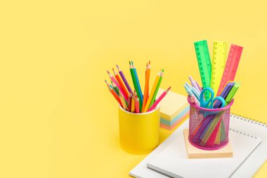 Kalemleri, kalemleri, kalemleri, makası ve cetvelleri olan iki bardak bir not defterinin sarı arka planında duruyor. Kopyalayacak bir yer. Reklamcılık, tasarım, mükemmel rötuş..