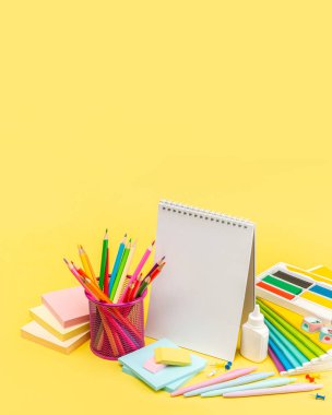 Kırtasiye malzemeleri. Renkli kalemler, bir defter, yapıştırıcı, plasticin, bir açıcı, bir kalem, notlar için bloklar ve sarı arkaplanda bir silgi. Kopyalayacak bir yer. Reklam ve tasarım için bir boşluk