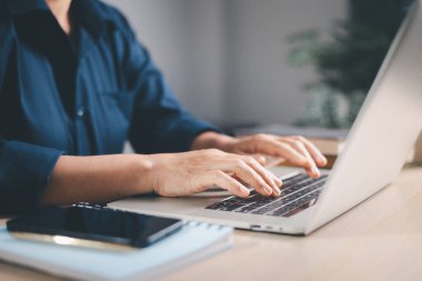 Ev telefonu ve not defteriyle dizüstü bilgisayar başında daktilo kullanan bir profesyonelin elleri. Sabah ışığı, uzaktan çalışmayı, üretkenliği, çevrimiçi iletişimi ve modern yaşam tarzını temsil ediyor..