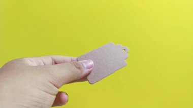 Bir el, sarı zemin üzerinde makas ile bir kağıt etiketi dikkatlice keserek, indirim stratejilerini, ani satın alma kararlarını ve görsel ipuçları ve promosyonların dürtüsel satın alma alışkanlıklarını resmediyor.