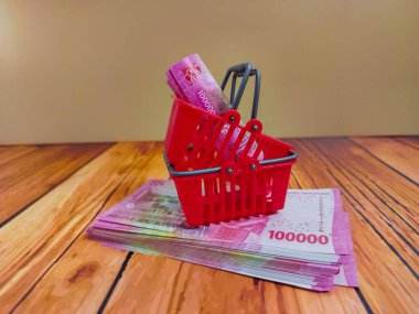 Ahşap bir yüzey üzerinde duran kırmızı bir mini sepet, alışveriş konseptini, bütçe farkındalığını ve paranın günlük alımlara nasıl aktığını gösteriyor.