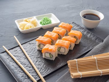 Suşi Philadelphia 'yı gri arka planda siyah desenli bir tabakta yuvarlıyor. Wasabi zencefili ve sos çubukları. Somon, krem peynir, avokado..