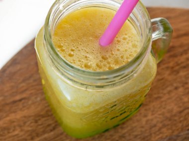 close-up of a yellow smoothie in a jar with a tube. The view from the top. Healthy sweet drink.