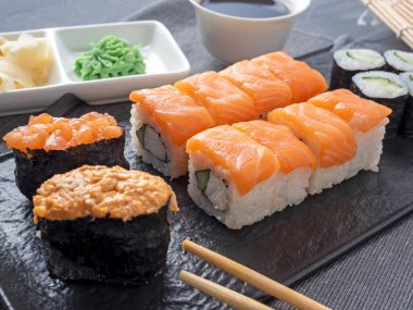 Siyah bir tabağa yerleştirilmiş çeşitli dürümler ve suşi Gunkan. Yanında bambu wasabi çubukları ve sos var. Yan görüş. Geleneksel Japon mutfağı