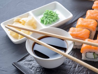 Suşi Philadelphia 'yı gri arka planda siyah desenli bir tabakta yuvarlıyor. Wasabi zencefili ve sos çubukları. Somon, krem peynir, avokado..