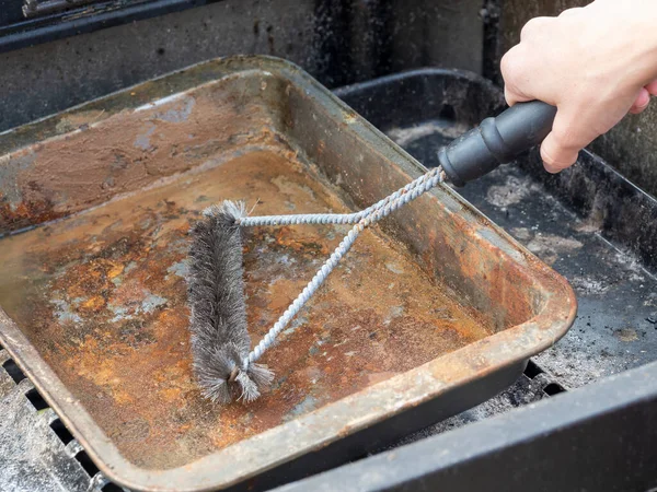 Cleaning a dirty grill pan with a metal brush. close up. horizontal image.