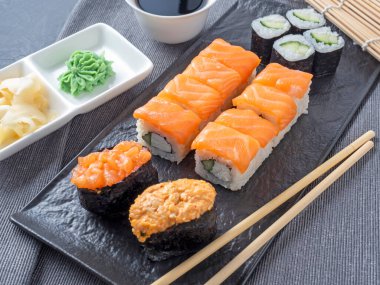 çeşitli Japon dürümleri ve dokulu bir tabakta suşi. Yan görüş. Yakınlarda zencefil ve sos çubukları var..