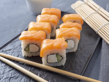 Philadelphia suşisi gri arka planda siyah desenli bir tabakta yuvarlanıyor. Yakınlarda bambu çubukları var. Yan manzara, Japon mutfağı.