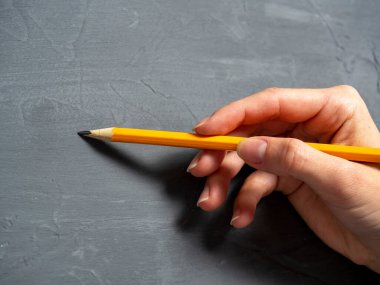 Gri dokulu arka planda bir kadının eli kalemi tutuyor. Yatay fotoğraf