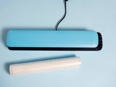 Parlak mavi arka planda mavi bir vakumlu paketleyicinin yakın çekimi. Paketleme çantalarının yanında. Ürünlerin tazeliğini koruyan bir makine. Düz yatış, üst görünüm.