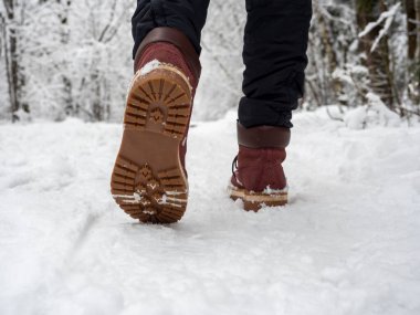 Botlu bir adam kış ormanında yürüyor. Ayakkabının alt görüntüsü, seçici odaklanma. Yürüyüş kavramı ve kış tatili