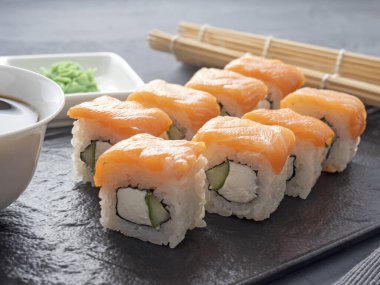 Suşi Philadelphia 'yı gri arka planda siyah desenli bir tabakta yuvarlıyor. Wasabi zencefili ve sos çubukları. Somon, krem peynir, avokado..