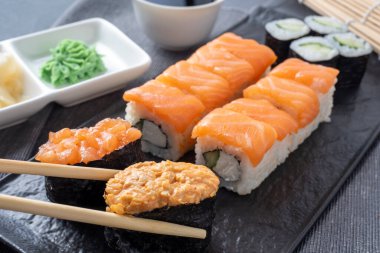 çeşitli Japon dürümleri ve dokulu bir tabakta suşi. Yan görüş. Yakınlarda zencefil ve sos çubukları var..