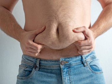 Kot pantolonlu adam kıllı, sarkık, şişman karnını sıkıyor. Yetersiz beslenme kavramı. Vücut pozitif. Kendini kabullenme