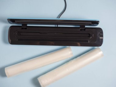 Parlak mavi arka planda mavi bir vakumlu paketleyicinin yakın çekimi. Paketleme çantalarının yanında. Ürünlerin tazeliğini koruyan bir makine. Düz yatış, üst görünüm.