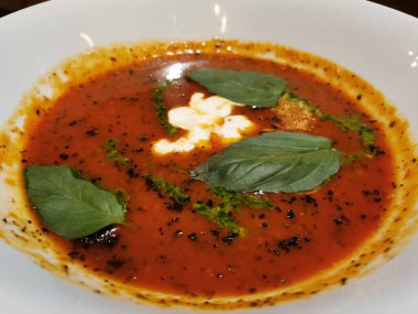 Fesleğen yapraklarıyla süslenmiş beyaz bir tabakta Stracciatella peynirli İtalyan domates çorbası.