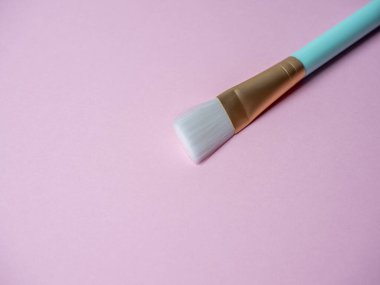 Yüz maskesi takmak için mavi bir kozmetik fırçası pembe arka planda yatar. Kozmetik aksesuarlar, metin için boşluk, kopyalama alanı
