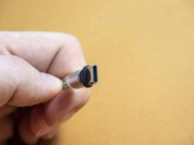 USB tip C kablosu, elinizde kahverengi bir fonda manyetik bir eklenti ile katlanabilir. Boşluğu kopyala