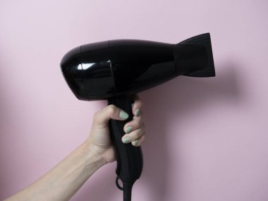 Pembe arka planda bir kadının elinde siyah saç kurutma makinesi. Saç Bakımı Ürünleri