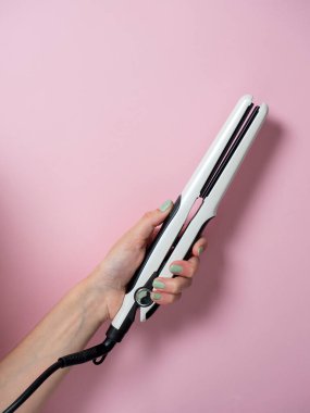 Beyaz saç maşası arka planda bir kadının elinde. Saç stili yaratmak için bir aksesuar. Güzellik ve moda. Saç bakımı.