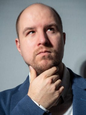 Ceket ve gömlek giymiş orta yaşlı bir adamın portresi. Düşünceli bir şekilde yukarı bakıyor. Bir el sakalını tutuyor. Duygular, düşüncelilik, iş adamı, sakal, saçlar.