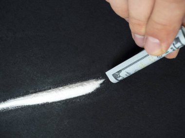 100 dolarlık banknotun yakın plan çekimi beyaz toz çizgisinin üzerinde bir tüpe sarıldı. Kötü alışkanlıklar, uyuşturucu kullanımı, ölüme yol açan yasadışı maddeler. Seçici Odaklanma