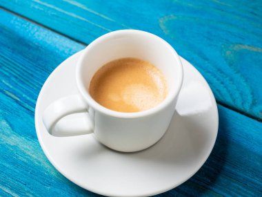 Bir fincan beyaz kahve tam espresso ile bir fincan çay tabağı ve mavi ahşap arka planda ayarlanır. Kahve, enerji içeceği. Nefis köpük.