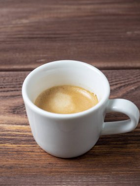 Ahşap zemin üzerinde lezzetli ve aromatik bir espresso olan beyaz bir fincan. Dikey fotoğraf, kenar görünüm
