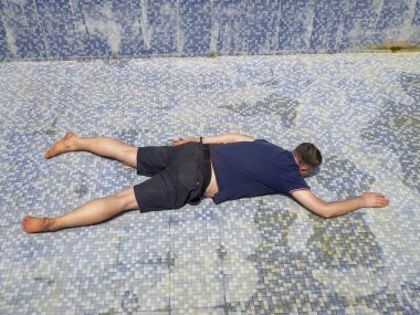 Elbiseli bir adam gün boyunca boş bir havuzda yatar ve yüzme numarası yapar. Şaka, rahatla.