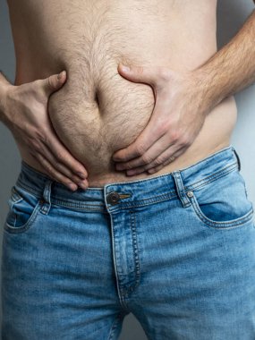 Kot pantolonlu adam kıllı, sarkık, şişman karnını sıkıyor. Yetersiz beslenme kavramı. Vücut pozitif. Kendini kabullenme, dikey fotoğraf