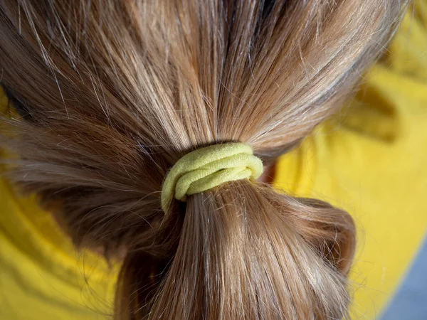 Close up of blonde hair tied in a bun with a yellow elastic band