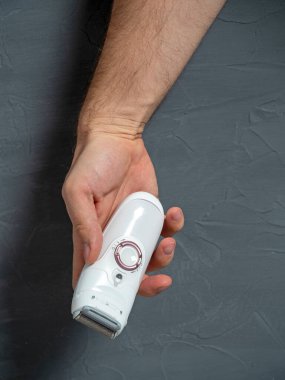 Bir adamın eli beyaz bir elektrikli epilatör tutuyor. Gri arka plan. Erkek güzeli. Özbakım, kozmetoloji. Yatay fotoğraf