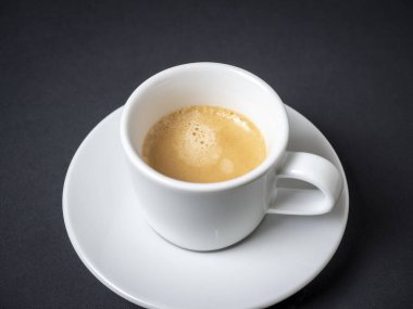 Bir fincan beyaz kahve tam espresso ile bir fincan çay tabağına ve siyah bir arka fona kurulur. Kahve, enerji içeceği. Nefis köpük.