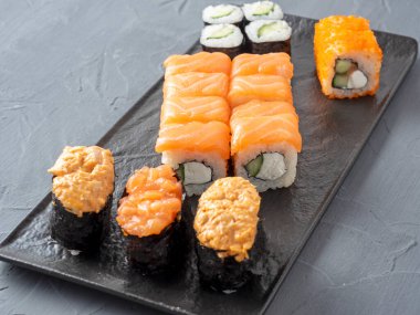 çeşitli Japon dürümleri ve siyah bir tabakta suşi. Yan görüş. Kapatın. Yiyecek bileşimi